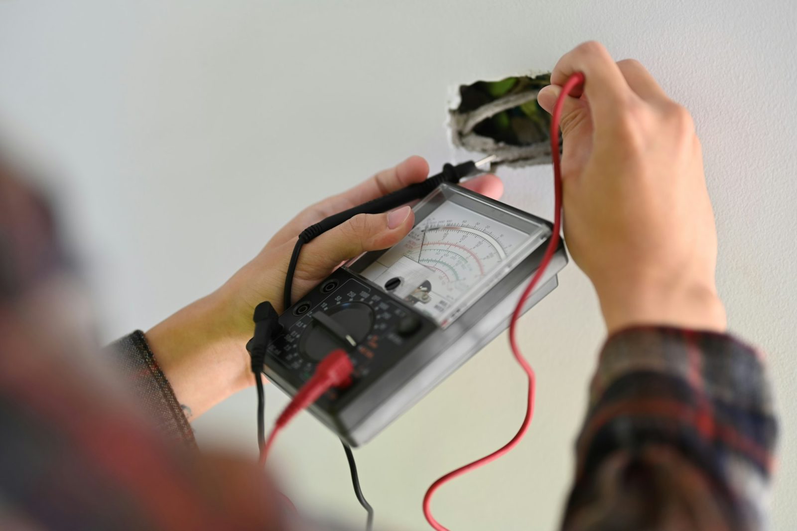 PAT Testing Electrician installer using a multimeter to test power line current in an electrical system.